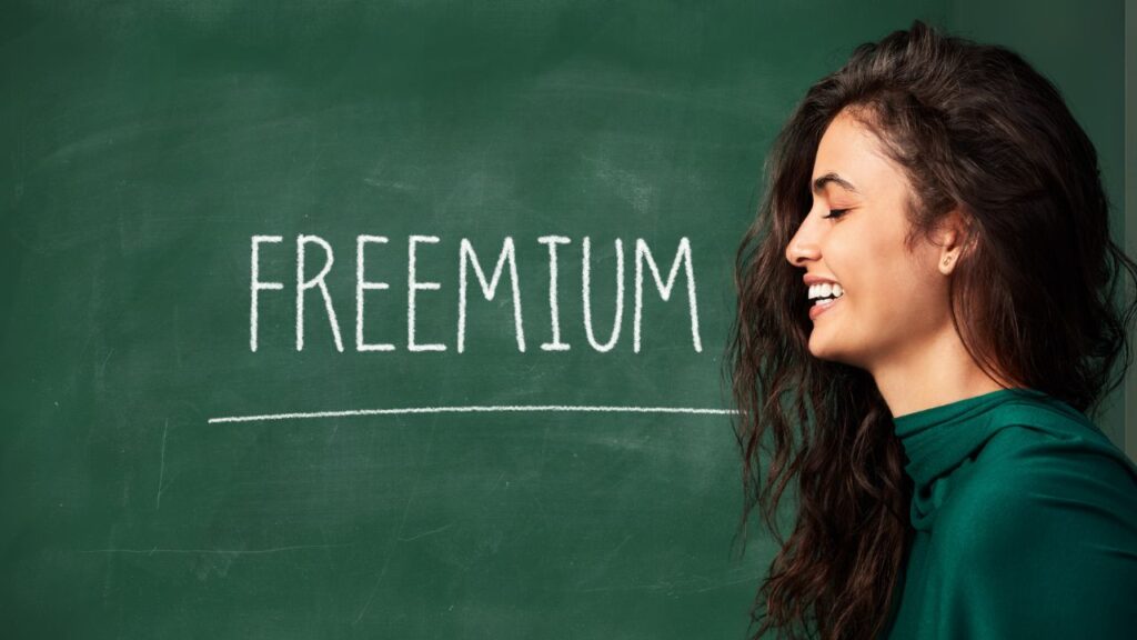 Mulher sorrindo em frente a um quadro verde com a palavra "freemium" escrita com giz — o que é freemium.