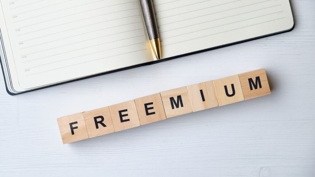 Blocos de madeira com a palavra "freemium" em destaque sobre uma mesa branca, ao lado de caderno e caneta — o que é freemium.