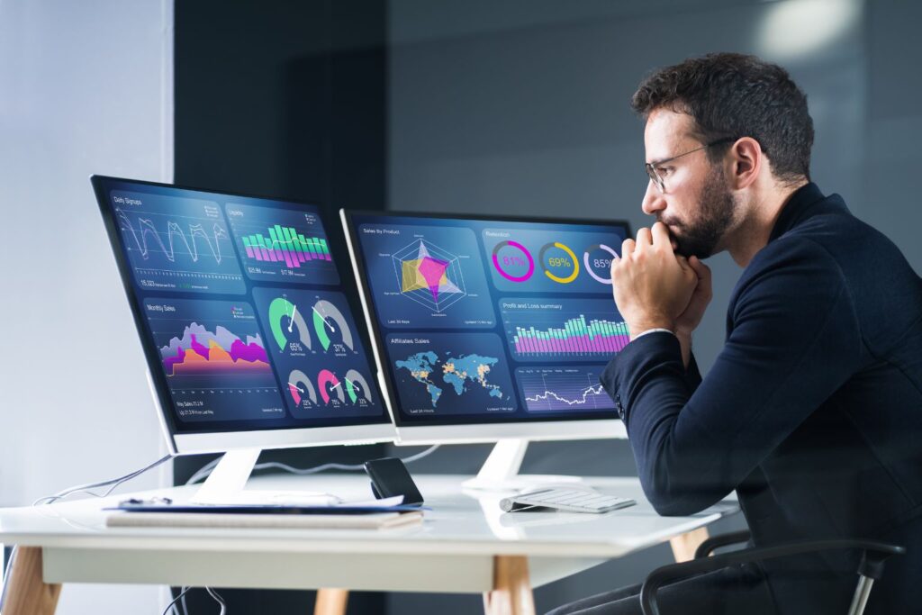 Analista observando dois monitores com gráficos e indicadores de web analytics