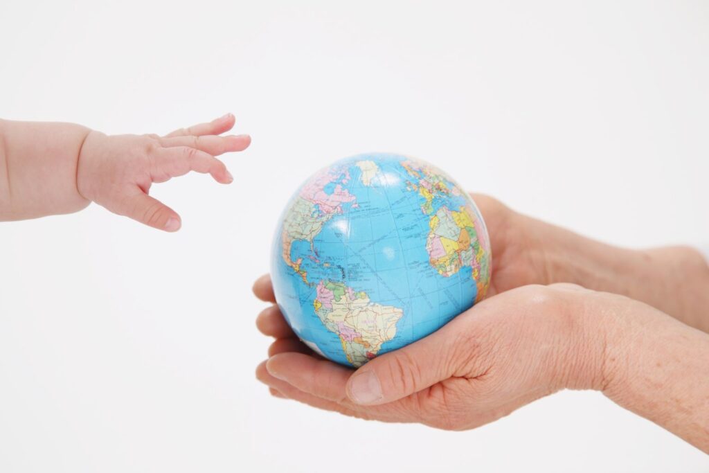 Mão de bebê alcançando um globo terrestre segurado por mãos adultas, simbolizando alcance orgânico