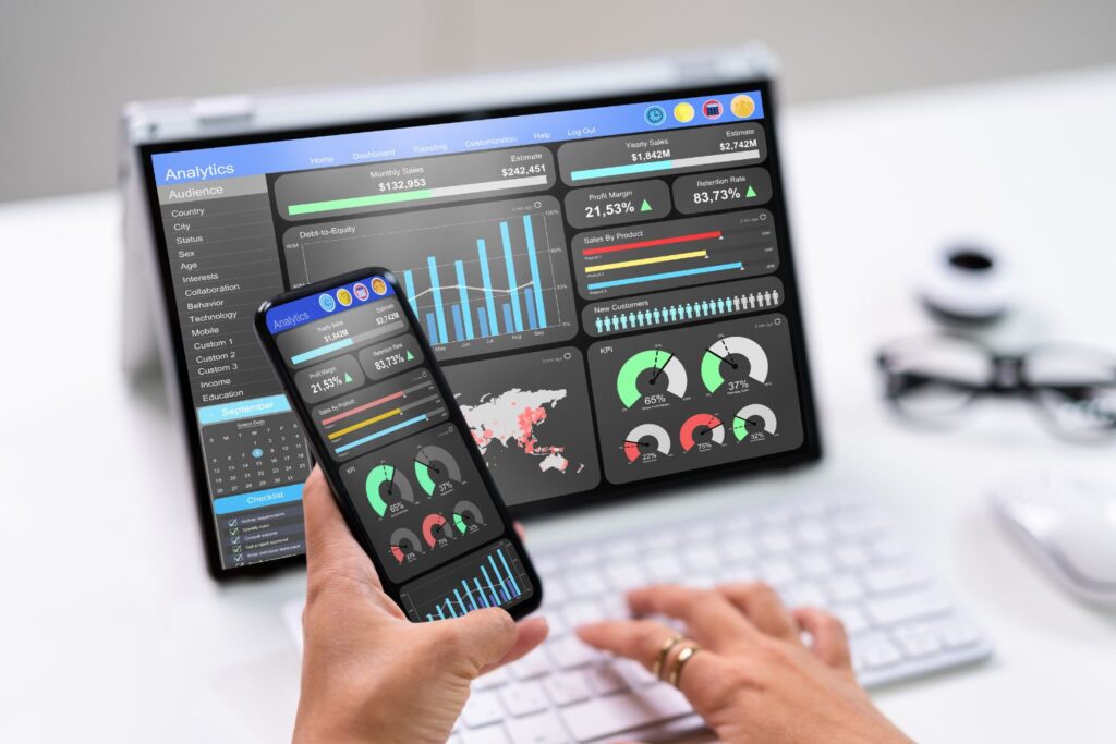Mãos usando smartphone e laptop exibindo gráficos e métricas em painel de web analytics