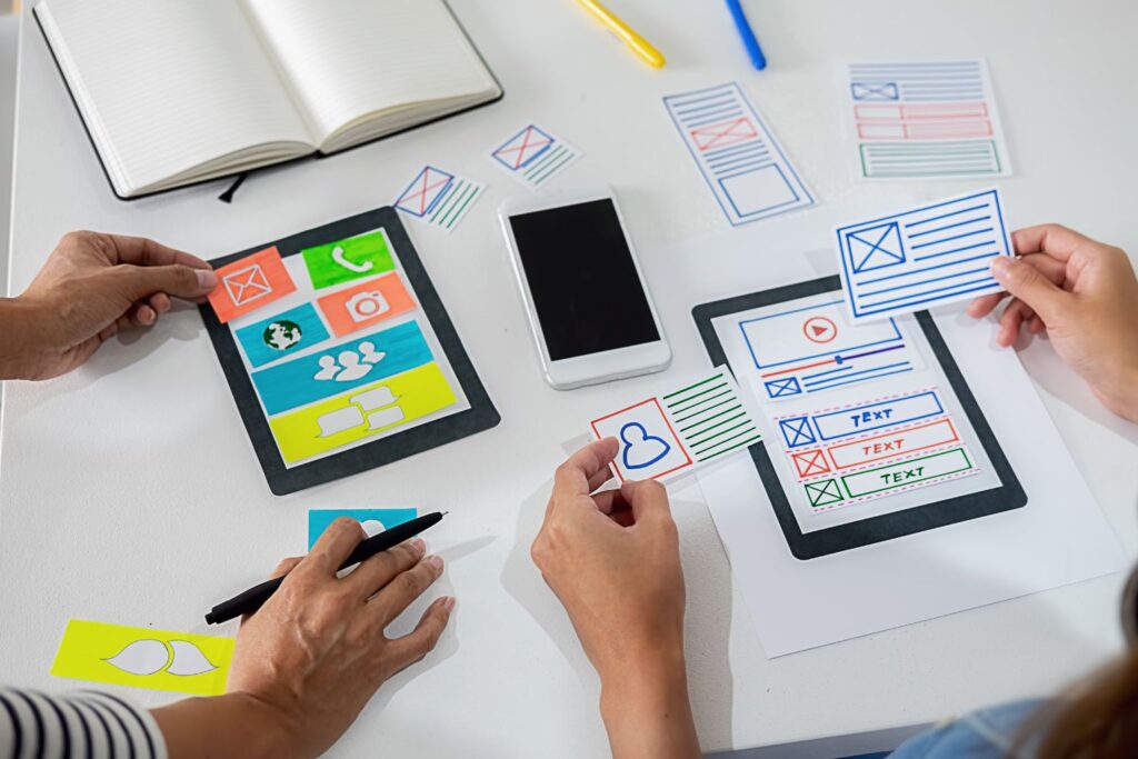 Duas pessoas organizando interface de aplicativo em mesa com ícones coloridos, representando agregador de conteúdo online
